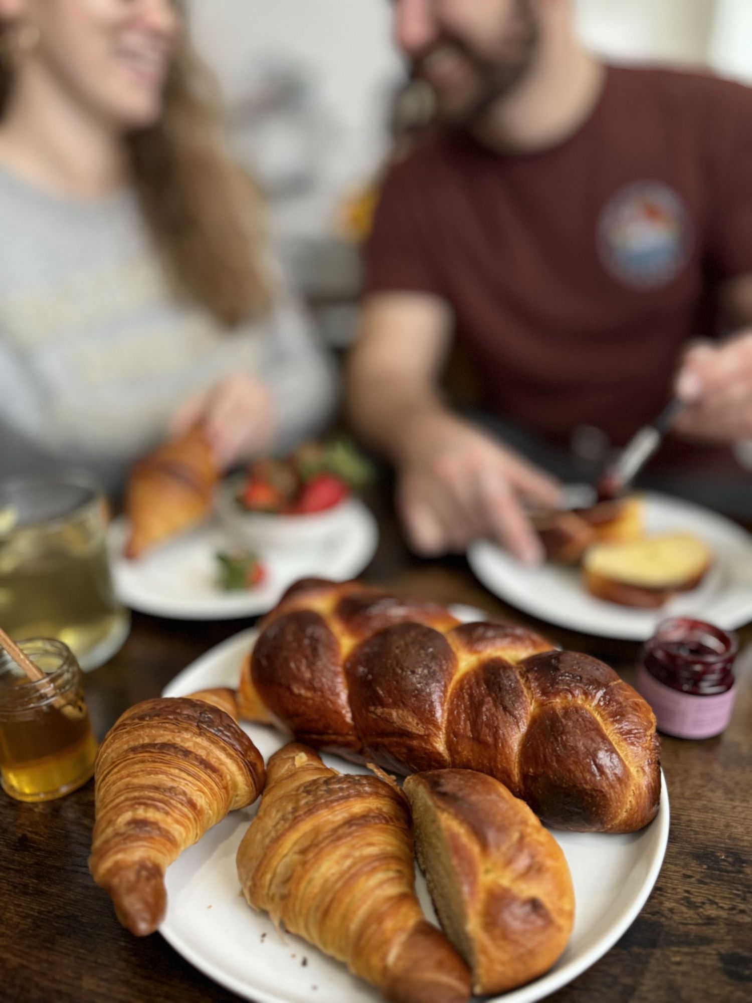 A couple sharing brunch at a table with golden croissants and a braided brioche