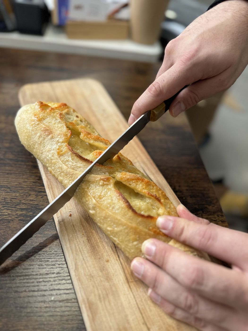 Hands slicing a freshly baked baguette on a wooden board